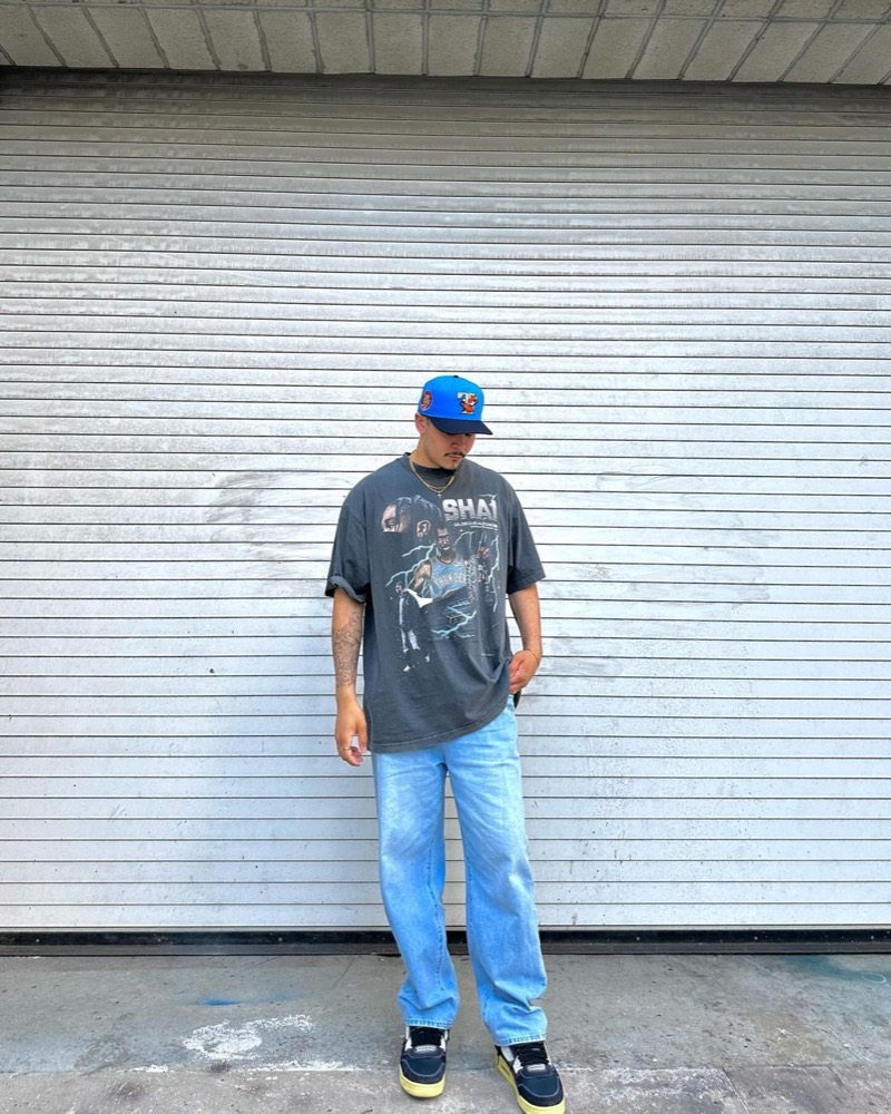 A man in a blue cap and a graphic tee standing in front of a grey roll-up door