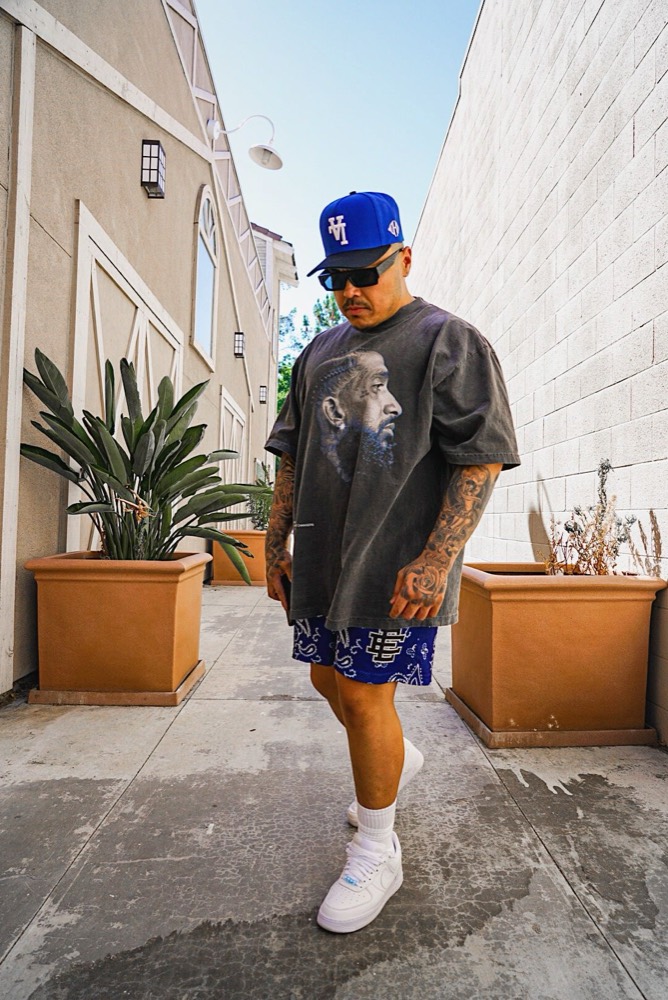 A man in a blue cap and a graphic tee walking along a sunny wall