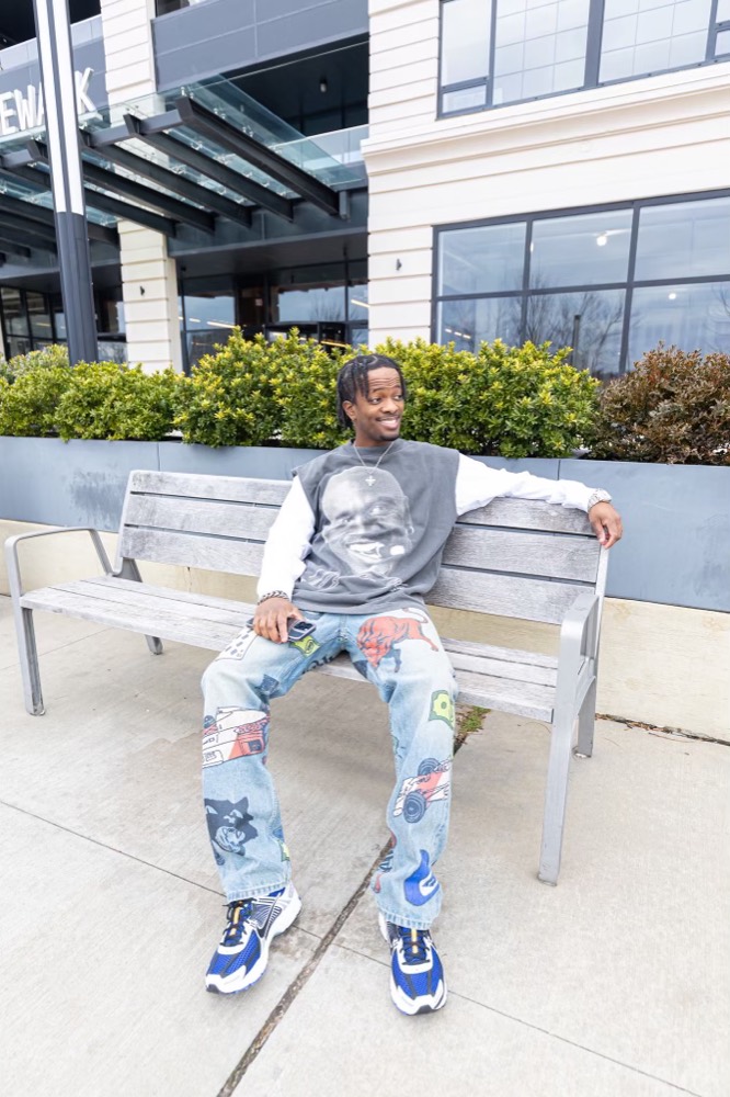 A man seated on a bench in a graphic tee and patchwork jeans