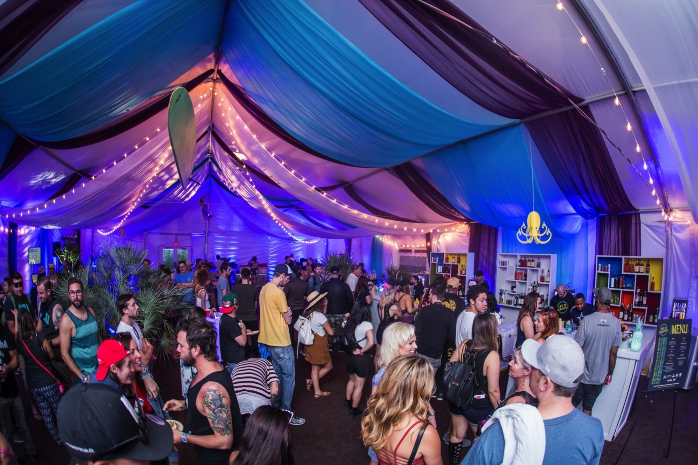 The same VIP tent packed with guests under blue and purple lighting
