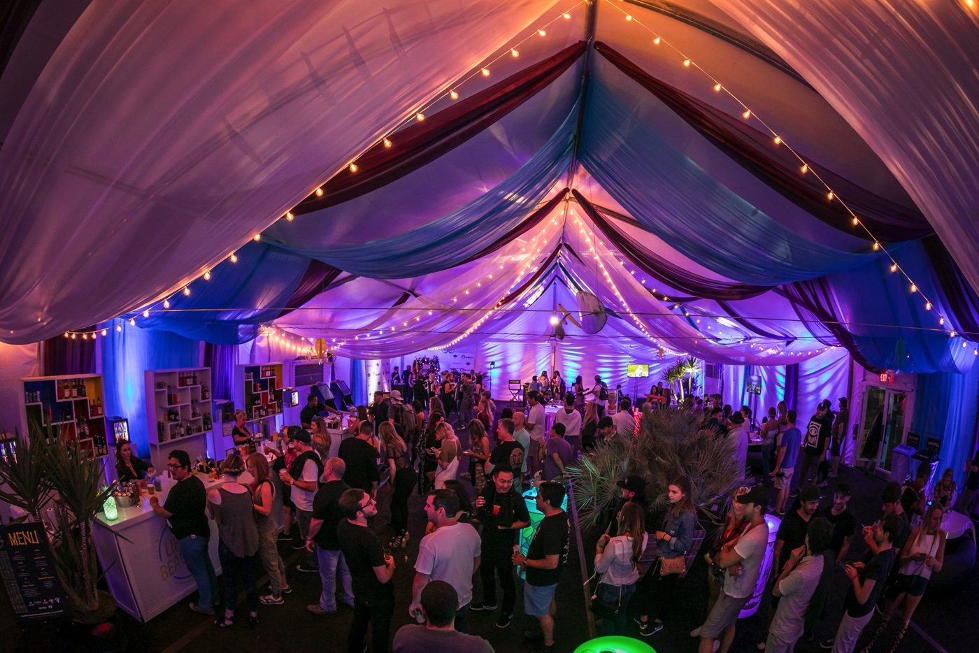 Wide view of the VIP tent full of guests under draped fabric and string lights