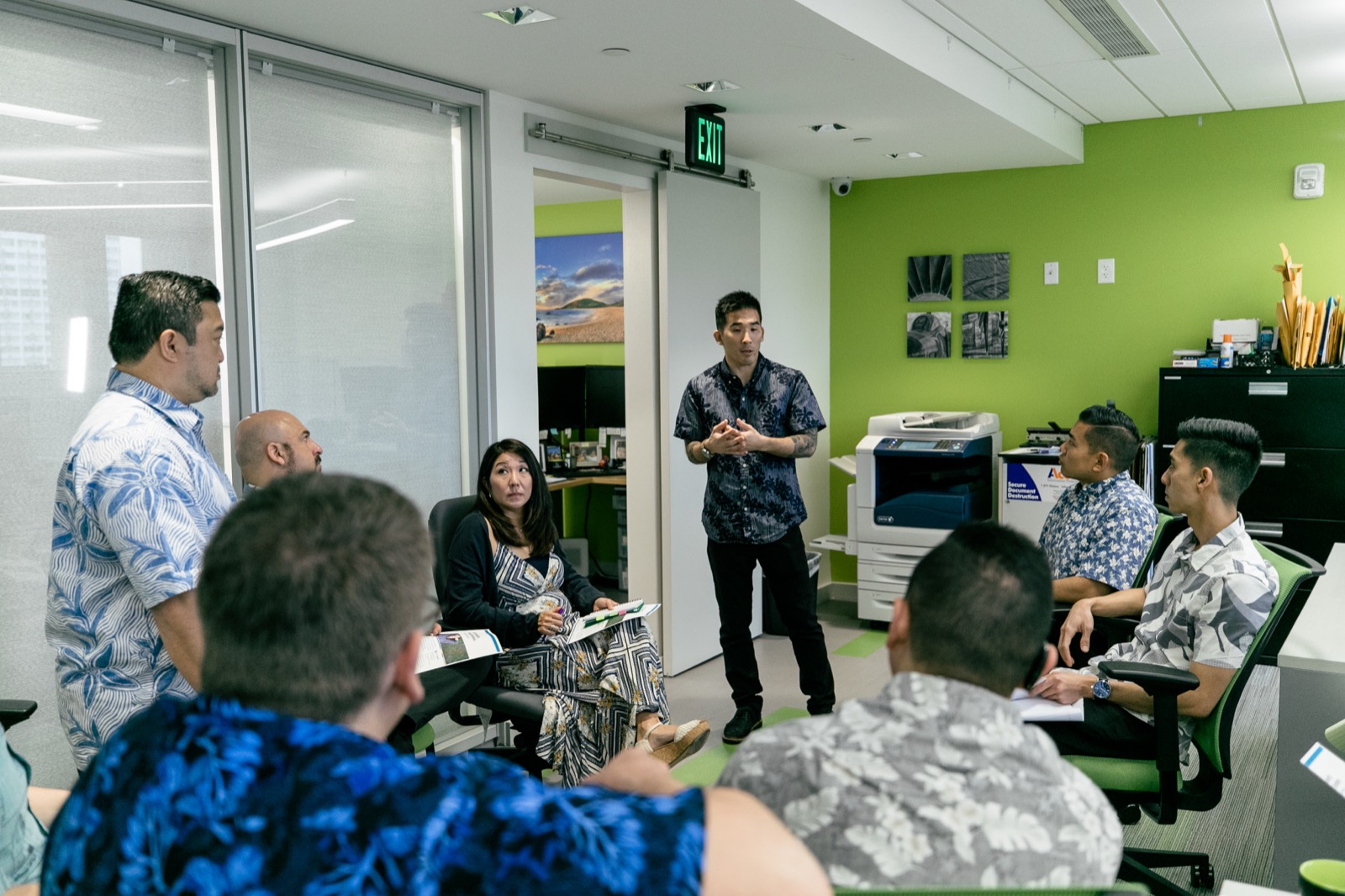 Tim Hirata standing to speak with a team seated around him in an office workshop